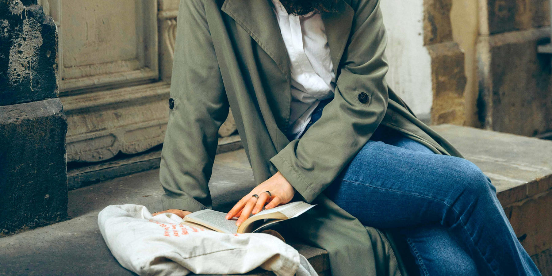 Frau sitzt dringend pinkeln müssend auf einer Treppe und liest ein Buch.