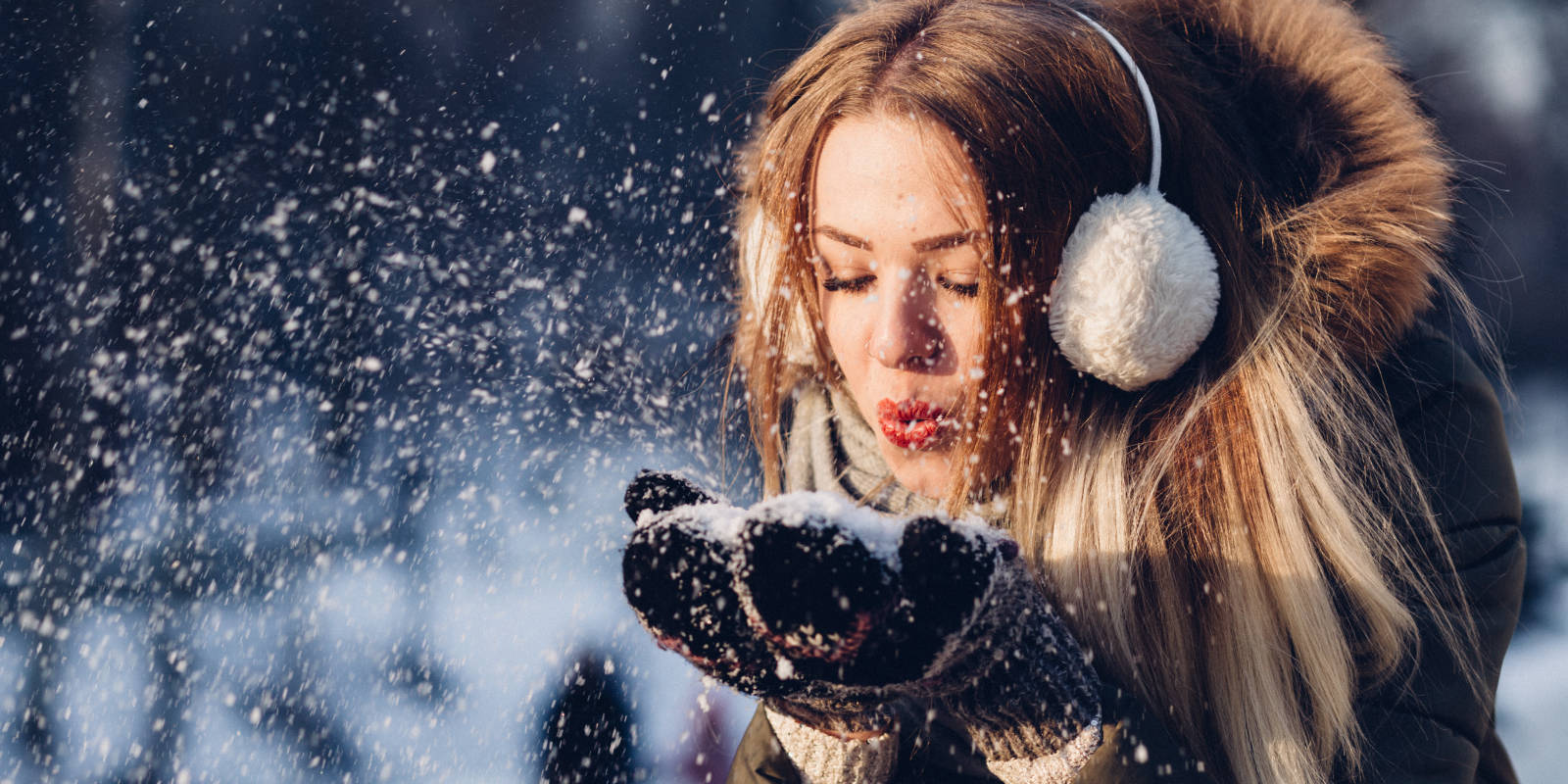 Junge Frau pustet vergnügt Schnee von ihren Handschuhen.